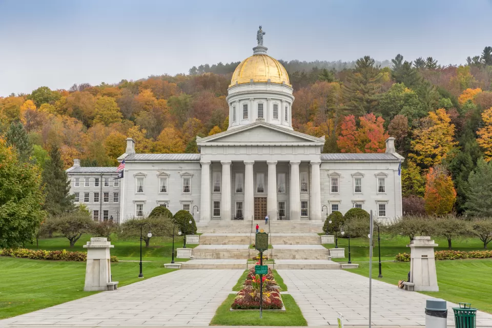 A picture of the Vermont State Capitol building with fall colors on display on trees in the background.